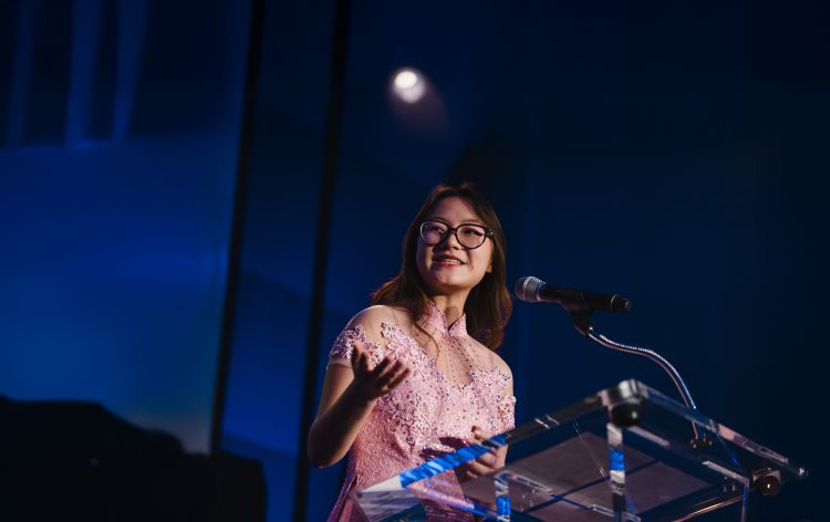 Smiling woman speaking at podium.